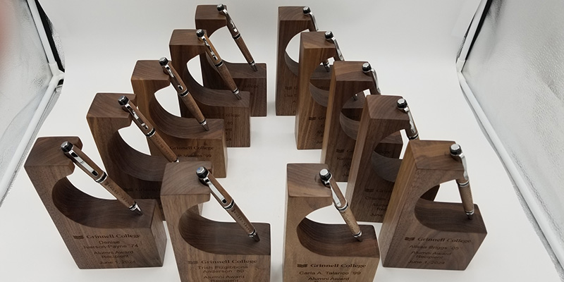 The 2024 Alumni Awards displayed on a table. The awards feature a wooden pen and a wooden holder created using trees removed during the building of the HSSC.