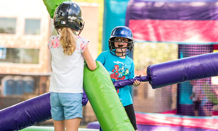 Two kids joust using foam jousting sticks while wearing helmets.