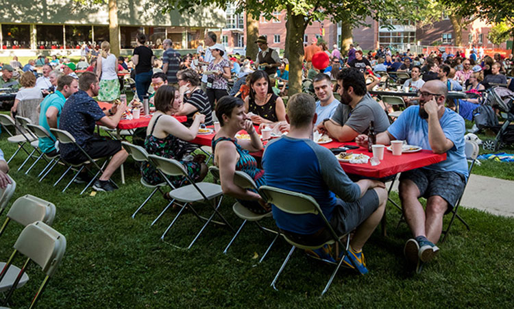 A group of alumni sit at long rectangular tables chatting and enjoying dinner.