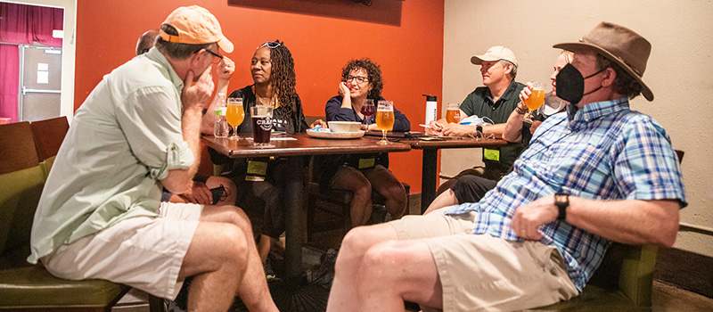 A group of alumni sit around a table with snacks and drinks during the Grinnell Pub Quiz.
