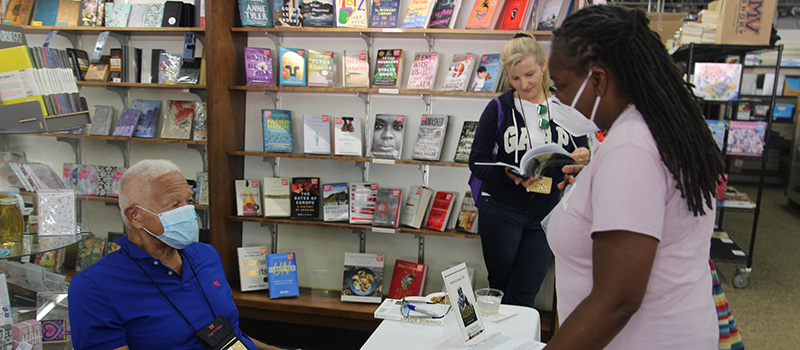 Jim Lowry ’61 sits at a table speaking with an alumnae at the Authors event at the Pioneer Bookshop.