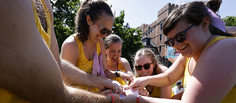 A group of young alumni smile and laugh as they try to unbunch a frozen t-shirt as a team.