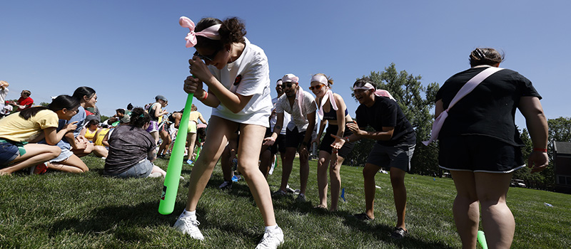 Alumni spin on a wiffle bat during a relay race.