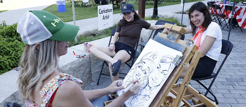Two young alumni get their caricature drawn.