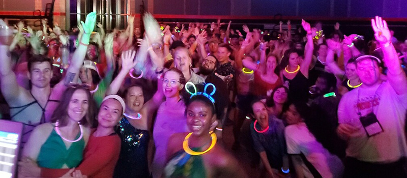 Alumni take a moment to pose for a group photo during Harris Party in glow sticks, violet lights, and club attire.