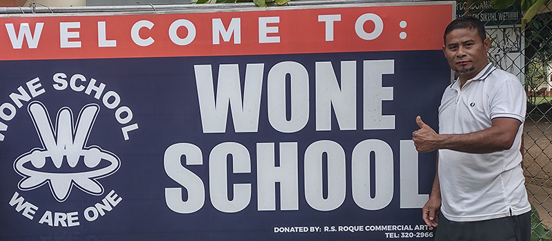 Wone School Principal Charles Armstrong stands next to a school sign.