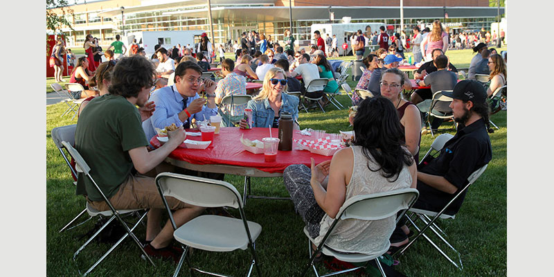 Alumni sit around a table during their class dinner after enjoying food from local food trucks.