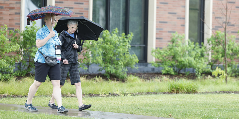 Two Reunion 2023 attendees walk with umbrellas in the rain.