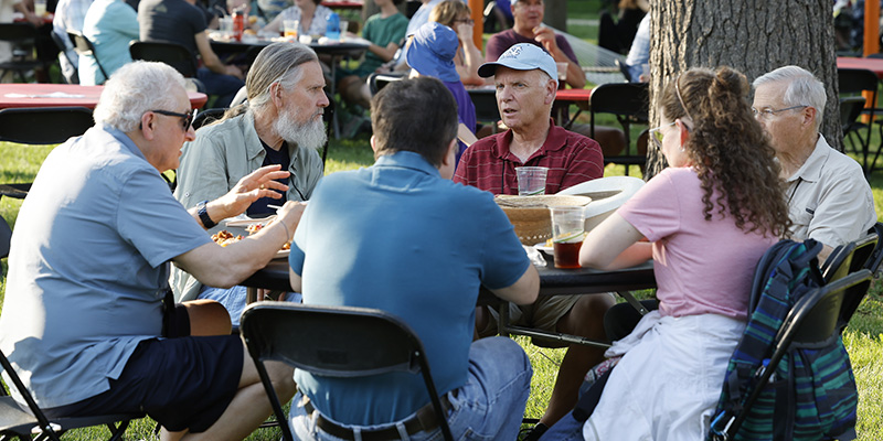 Alumni sit around a table catching up over food and drinks.