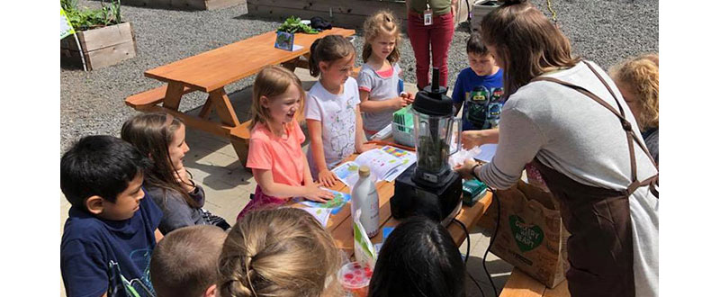 Students huddle around a demonstration of how to make smoothies from fresh produce.