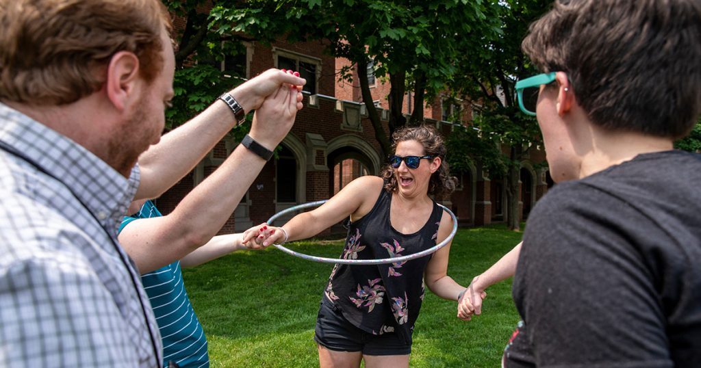 Grinnellians play a relay game trying to move a hula-hoop while their arms are connected.